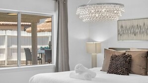 A hotel room with a large bed, a chandelier, a view of the outside patio, and a painting on the wall. - Best value,location, gameroom, pool+good size yard (Bermuda Dunes)