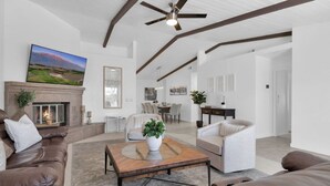 A spacious living room with a fireplace, leather sofas, a wooden coffee table, and a dining area in the background. - Best value,location, gameroom, pool+good size yard (Bermuda Dunes)