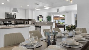 A modern kitchen with white cabinetry, a central island, and a dining area set for six with a buffet setup. - Best value,location, gameroom, pool+good size yard (Bermuda Dunes)