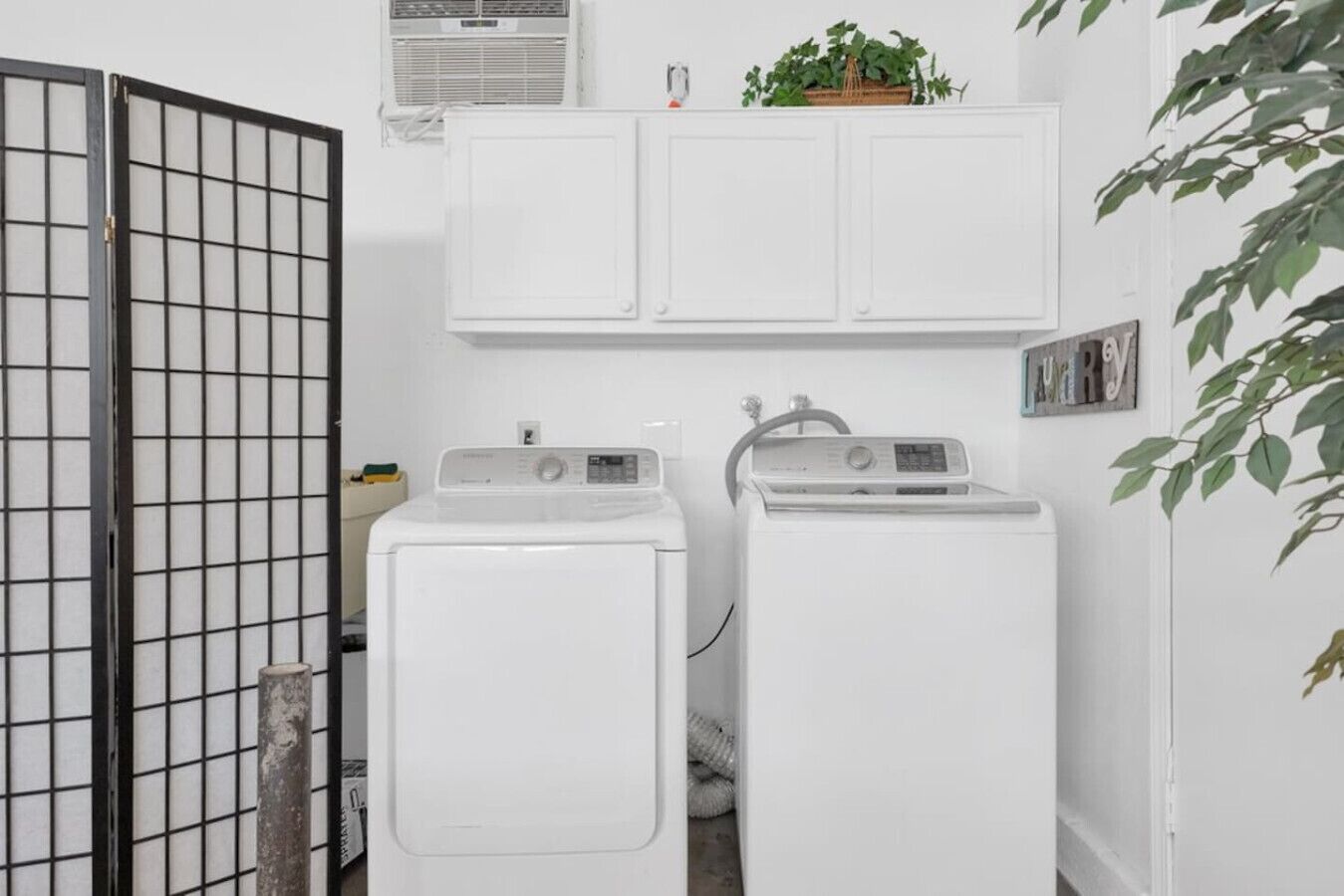 A laundry room with two front-loading washing machines, a drying rack, and a small shelf with a plant.