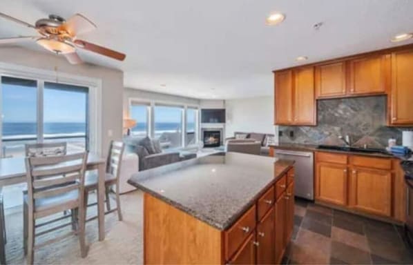 A modern kitchen with wooden cabinets, a granite countertop, and a view of the ocean.