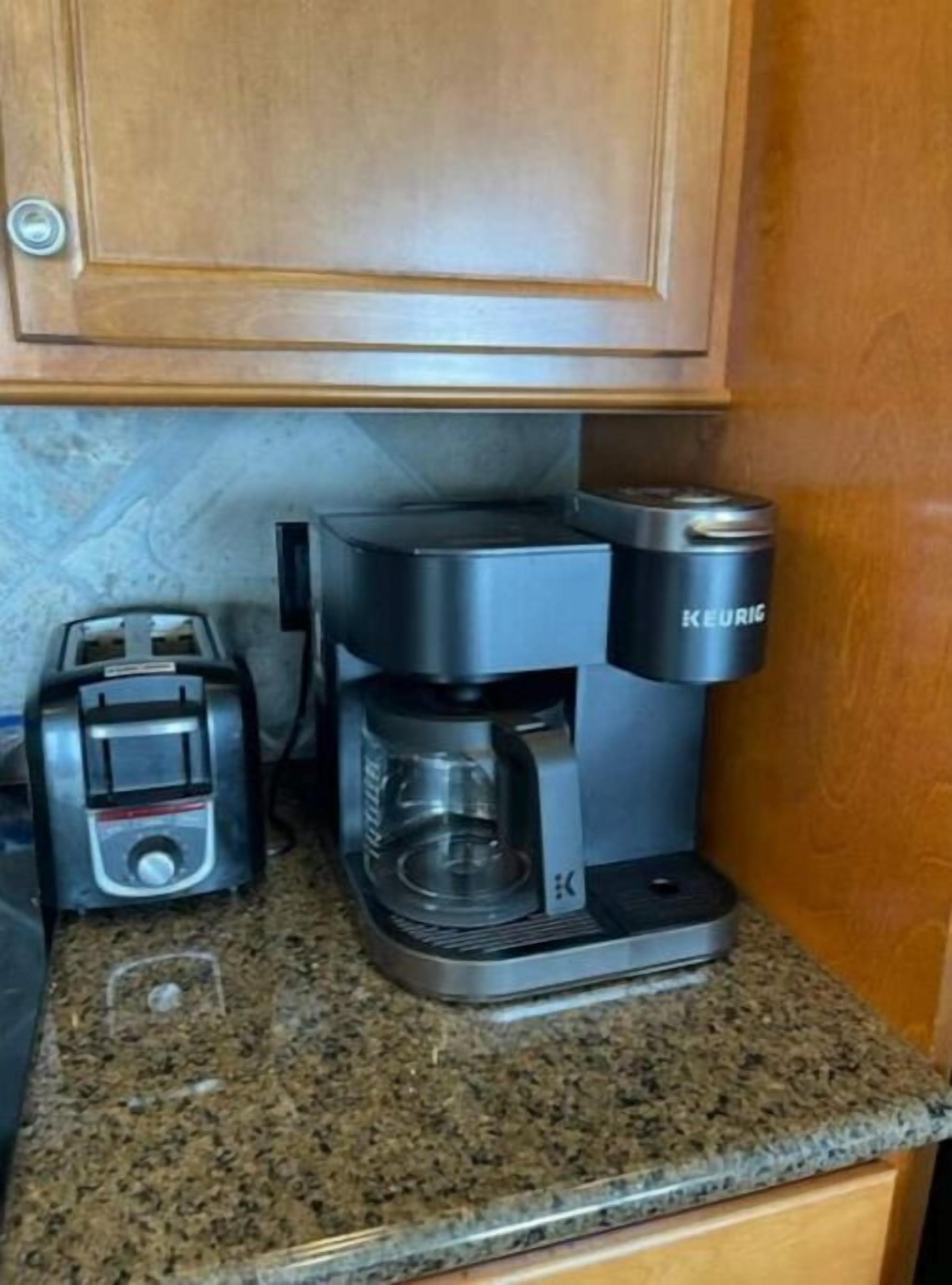 Een koffiezetapparaat op een granieten aanrecht, met een broodrooster en een houten kast erboven.