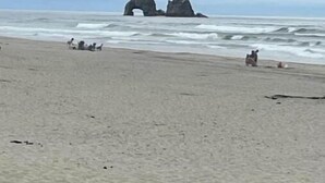 Una playa con rocas grandes en primer plano y una formación rocosa natural al fondo.