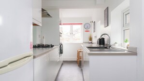 A narrow kitchen with white cabinets, a stainless steel sink, and a window with a view of buildings outside. - 3 Glendowne Terrace (Harrogate)