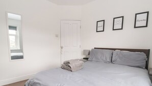 A bedroom with a bed, a bedside table, a lamp, a door, and a mirror. - 3 Glendowne Terrace (Harrogate)