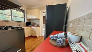 A compact kitchen with a stove, microwave, and a small sink. There is a red mat on the floor, and a black refrigerator. - Hill top view house, high speed wifi, Netflix & Prime Video (Sunbury)