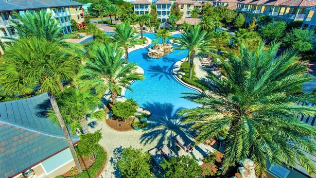 Un resort con piscina central, rodeado de palmeras y edificios de varios pisos con balcones.