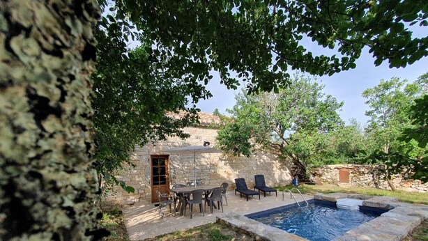 Ein Steinhaus mit Pool, Außenbereich mit Sitzgelegenheiten und einem Baum, der Schatten spendet.