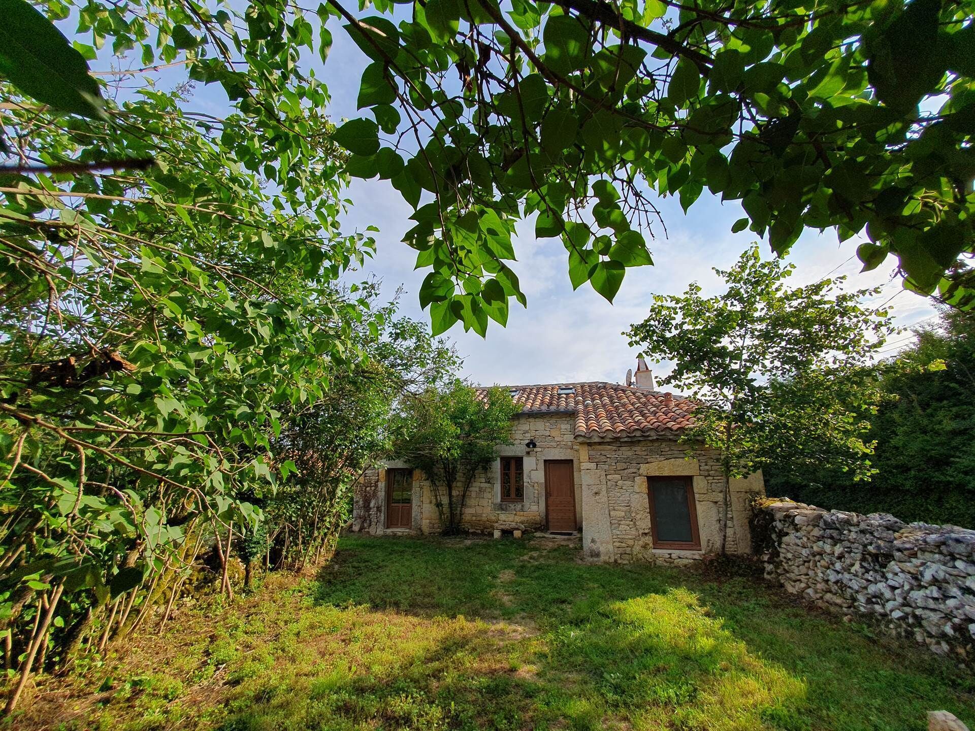 A stone house with a tiled roof, surrounded by greenery and a stone wall.