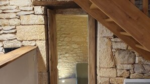 Ein rustikaler Raum mit Steinwänden und einer Holztreppe, die zu einem Erker führt.