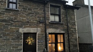 A stone building with a dark wooden door, a lit window, and a sign reading "Glan William". - Glan William (Dolwyddelan)