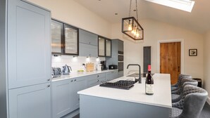 A modern kitchen with grey cabinets, a central island, and a wine bottle. - Glan William (Dolwyddelan)