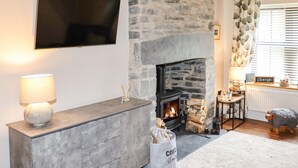 A living room with a stone fireplace, a flat-screen TV mounted on the wall, a sideboard with a lamp, and a cozy rug. - Glan William (Dolwyddelan)