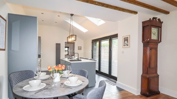 A dining area with a round table, grey upholstered chairs, and a chandelier. - Glan William (Dolwyddelan)
