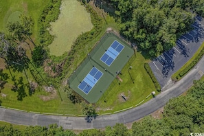 Vista aérea de una cancha de tenis rodeada de vegetación y un estacionamiento.