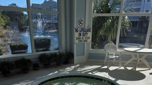 Piscina interna com aviso de ausência de salva-vidas, uma cadeira e uma mesa.