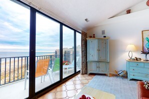Enjoy a room with a balcony offering a beach view, featuring a sliding glass door, a light blue cabinet, a table, and a chair.