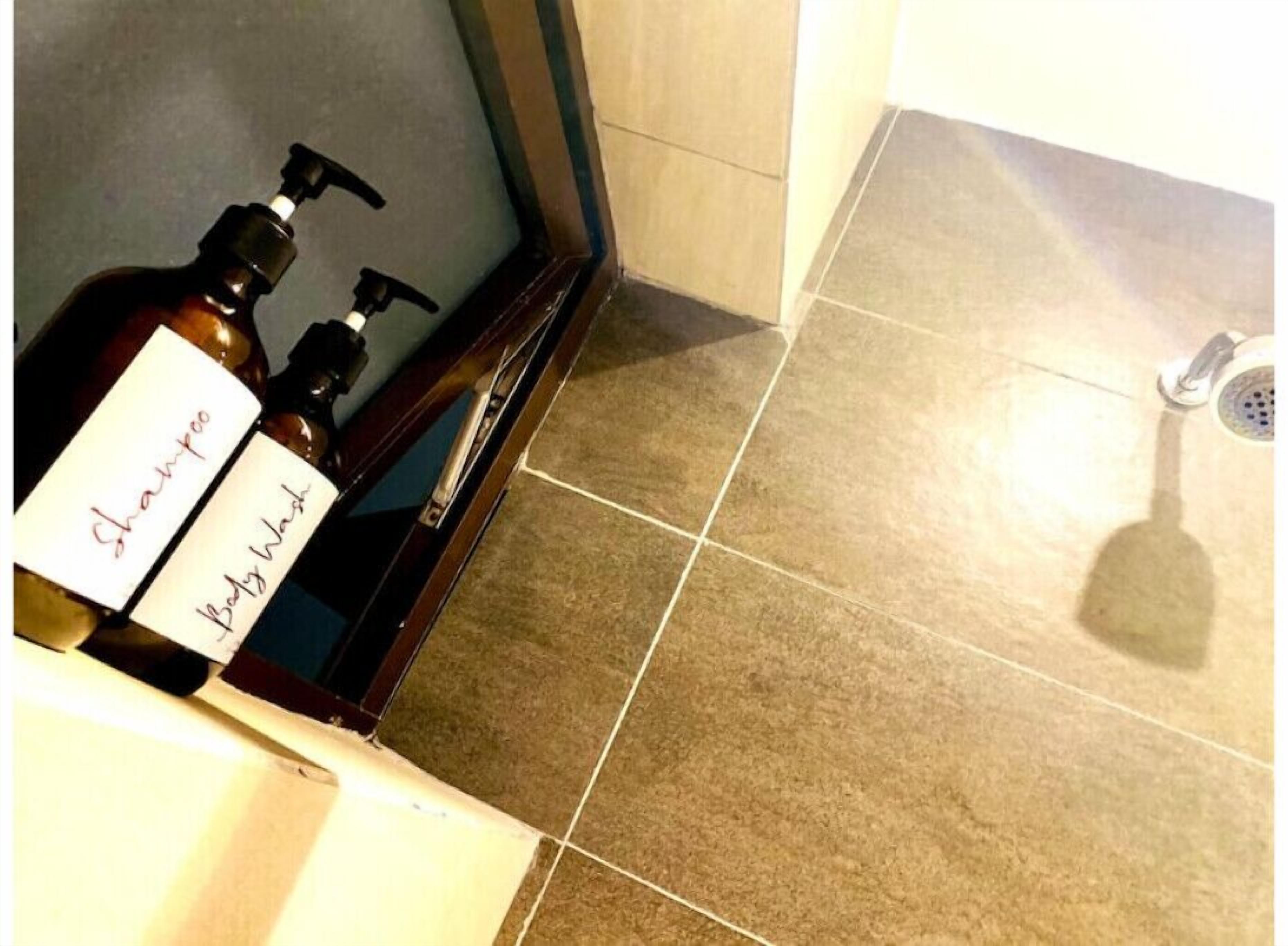 Une salle de bain avec un sol carrelé, une douche et deux bouteilles étiquetées « shampoing » et « gel douche » posées sur une étagère.
