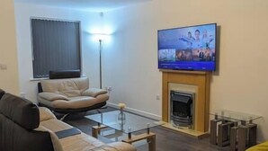 Un soggiorno moderno con un divano in pelle, un tavolino in vetro, un camino e un televisore a schermo piatto montato sopra.