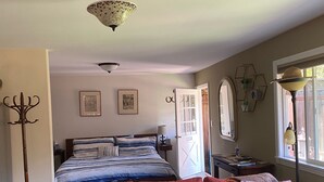 Quarto com cama, um sofá colorido, luminária de pé, espelho e janela com vista.