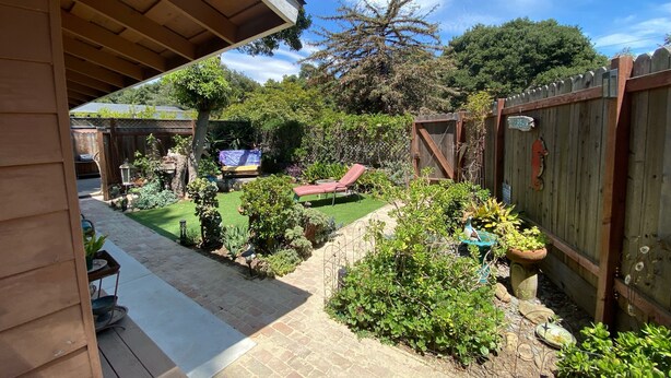 Um jardim com gramado, um deck de madeira e uma área cercada com um banco e uma mesa.