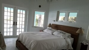 A bedroom with a large bed, two windows, and a door.