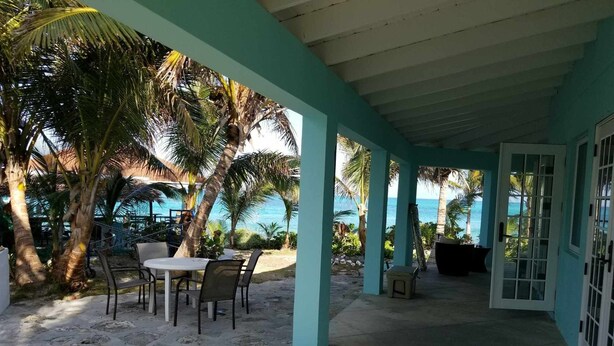 A covered outdoor area with a table and chairs, palm trees, and a view of the ocean.