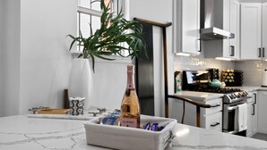 A modern kitchen with white cabinets, a marble countertop, a bottle of champagne, and a decorative plant.