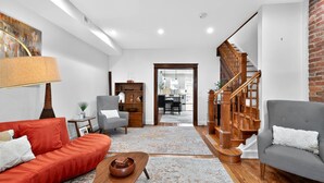A spacious living room with a red sofa, grey armchair, and a wooden coffee table. A staircase with wooden railings leads to an upper floor.
