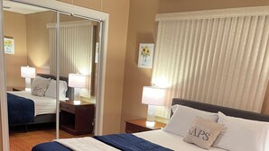Ein ordentlich eingerichtetes Schlafzimmer mit Bett, Nachttischen, einem Spiegel und einem Deckenventilator.