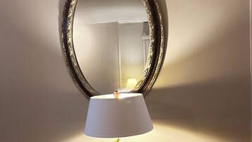 A table with a lamp and a mirror on a glass-top table against a wall.