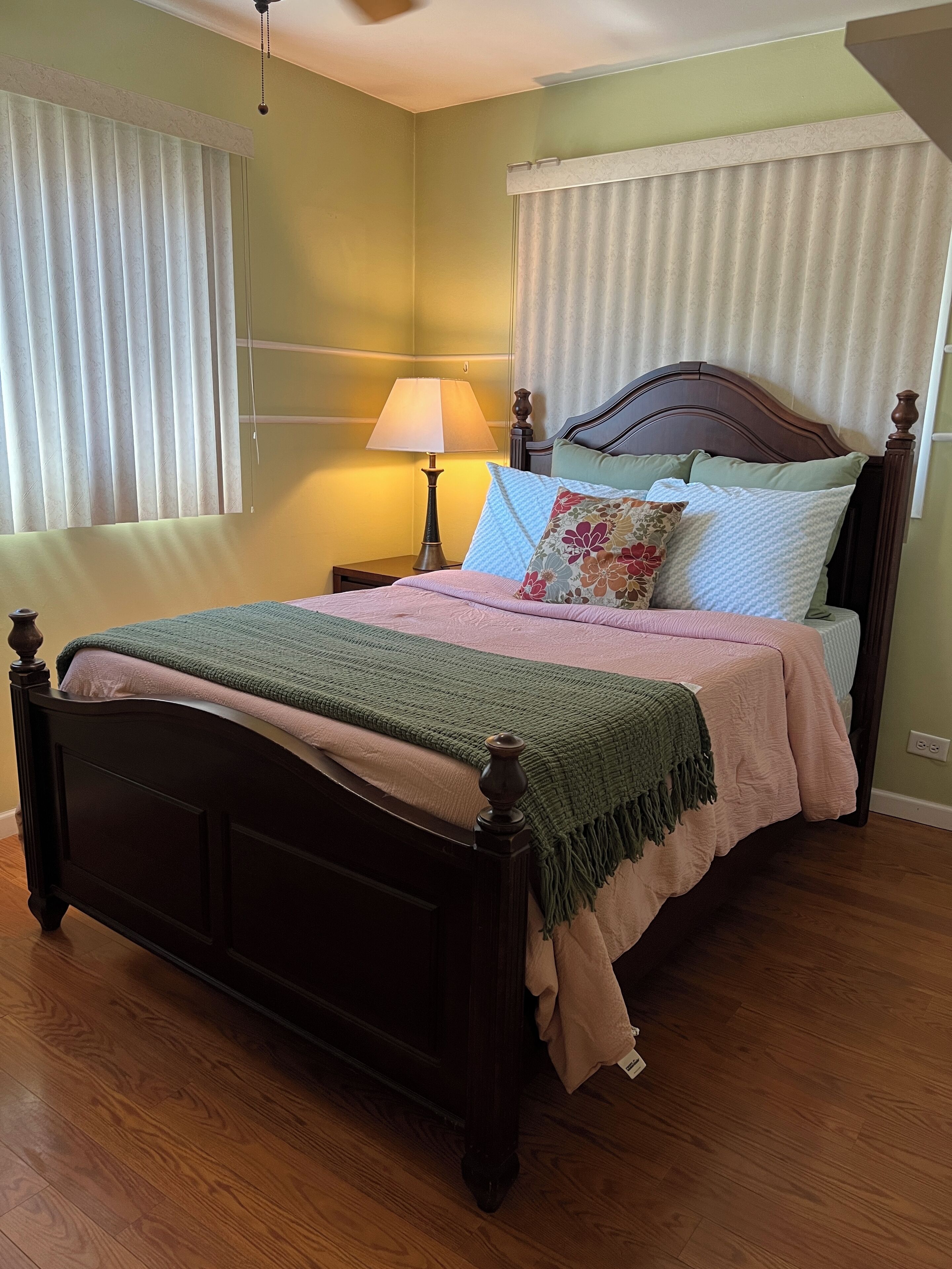 A neatly made bed with a wooden headboard, a bedside lamp, and a green throw blanket.
