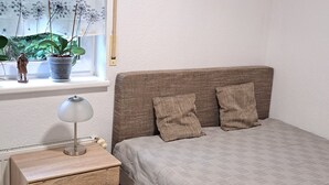 A bedroom with a bed, a dresser, a lamp, and a window with blinds.