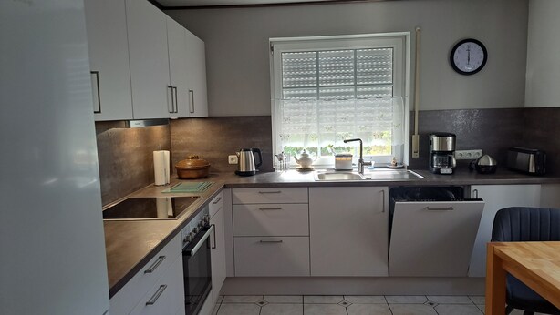 A modern kitchen with white cabinets, a built-in oven, a sink, and a window with blinds.