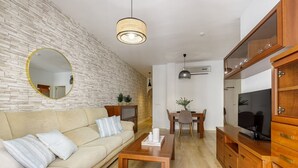 Un salon moderne avec un mur en briques, un miroir rond, un canapé, une table basse en bois et un téléviseur posé sur un meuble en bois.
