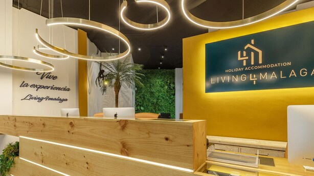 Un espace d’accueil avec un bureau en bois, un mur orné d’une affiche portant l’inscription « Vive la experiencia Living Analog » et une autre affiche indiquant « Holiday Accommodation Living4Malaga ».