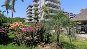 A multi-story hotel with balconies, surrounded by lush greenery and flowering plants.