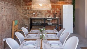 A dining area with a brick wall, a hanging light fixture, a white refrigerator, and a table set for six with white chairs. - Vacation home Rita by Interhome (Malgrat de Mar)