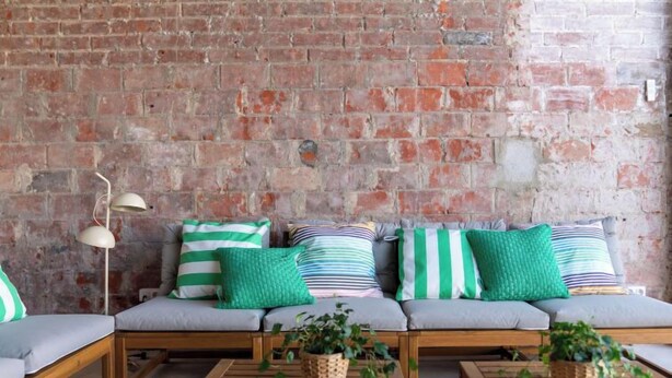 A cozy seating area with a brick wall, a sofa with striped cushions, and wooden tables. - Vacation home Rita by Interhome (Malgrat de Mar)