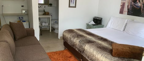 Un dormitorio con cama, sofá y baño visible a través de una puerta abierta.