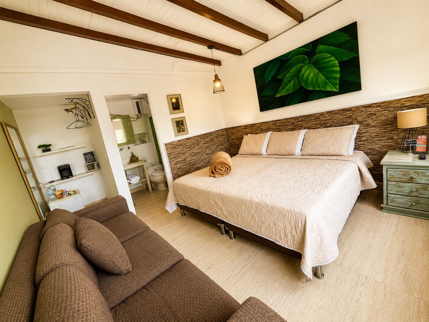 Una camera da letto con un letto, un divano marrone, un soffitto in legno, un muro in pietra e un quadro con una foglia verde.