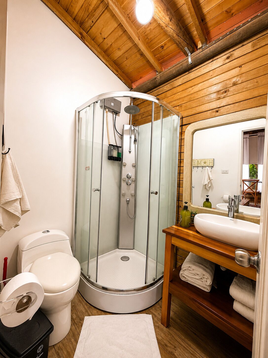 A compact bathroom with a glass-enclosed shower, a toilet, and a sink with a mirror.