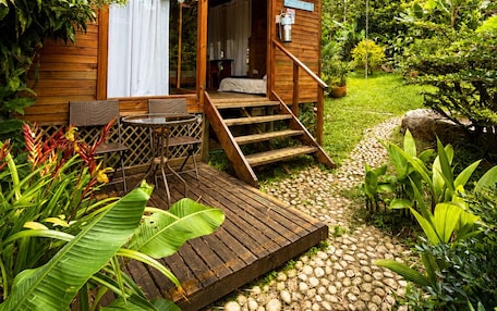 A wooden cabin with a porch, a dining area, and a staircase leading to the entrance.