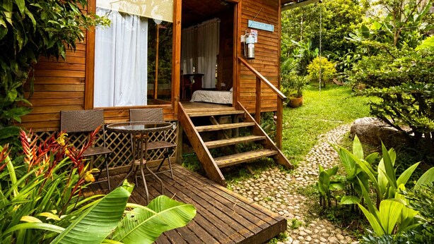 A wooden cabin with a porch, a dining area, and a staircase leading to the entrance. - HOTEL CASA MADERO (Envigado)