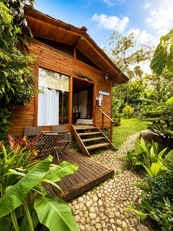 A wooden cabin with a porch, a dining area, and a staircase leading to the entrance.