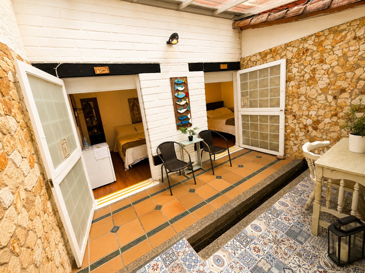 Una habitación con cama, una pequeña mesa con sillas, una planta en maceta y una pared decorada con peces.