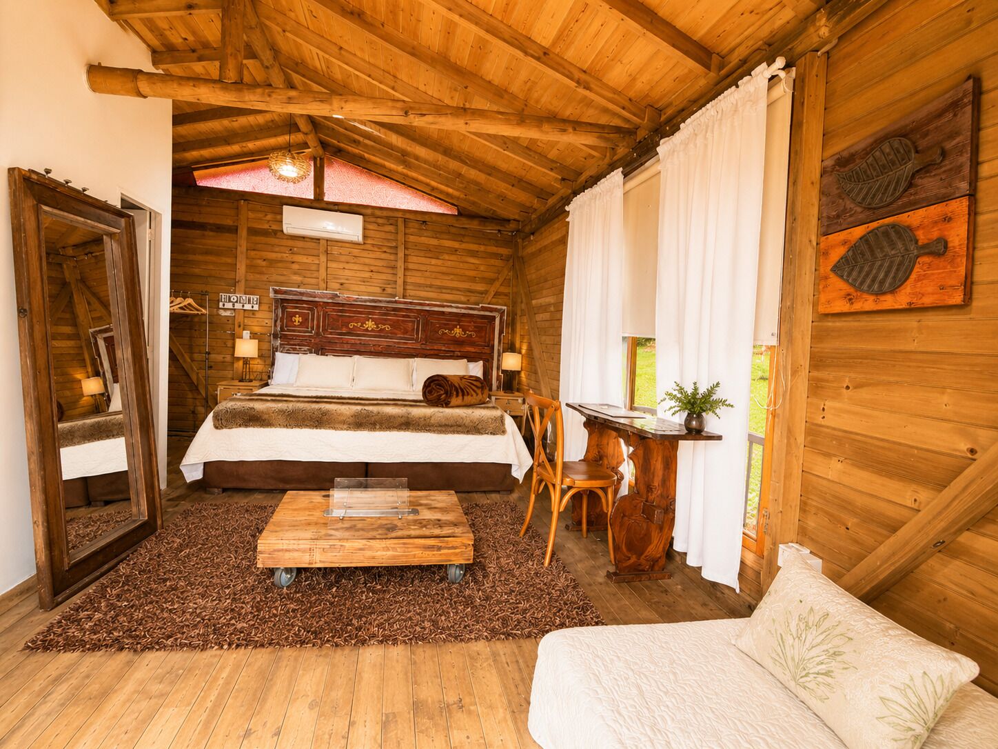 A wooden cabin bedroom with a bed, a small table, a chair, and a sofa.