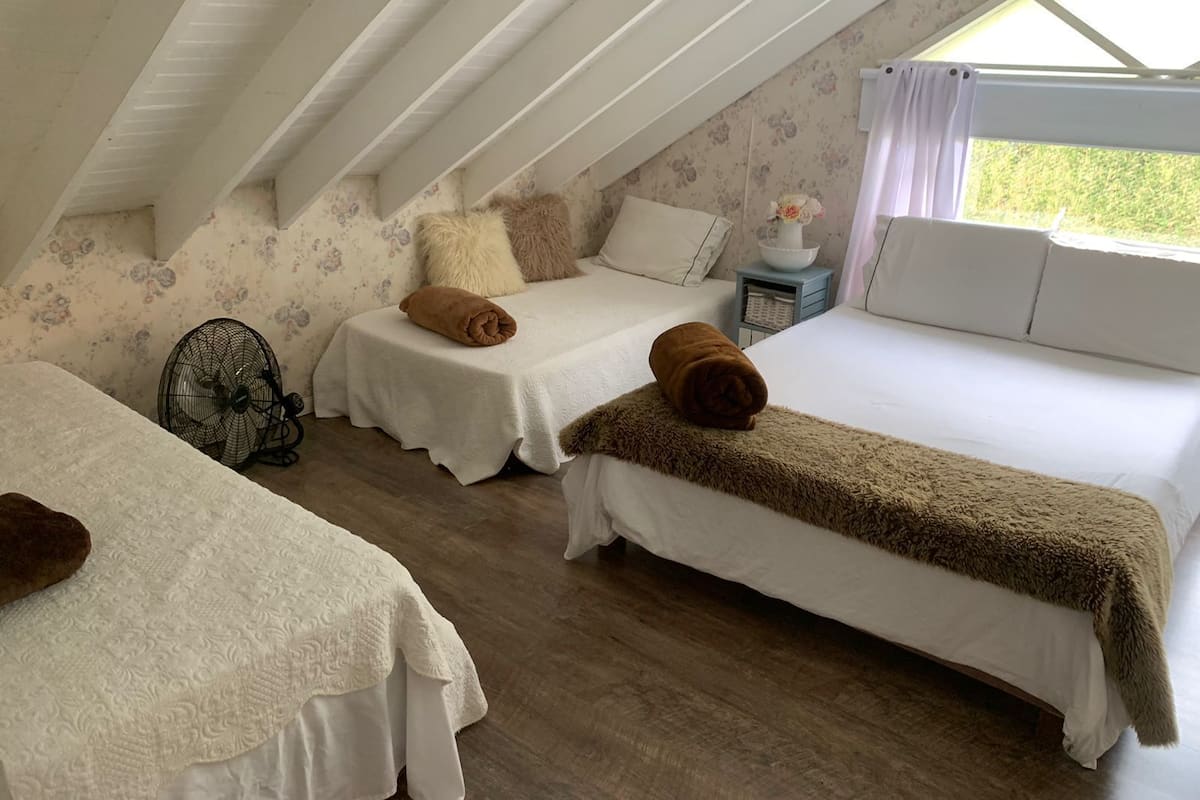 A cozy attic bedroom with two beds, a fan, and a window with curtains.