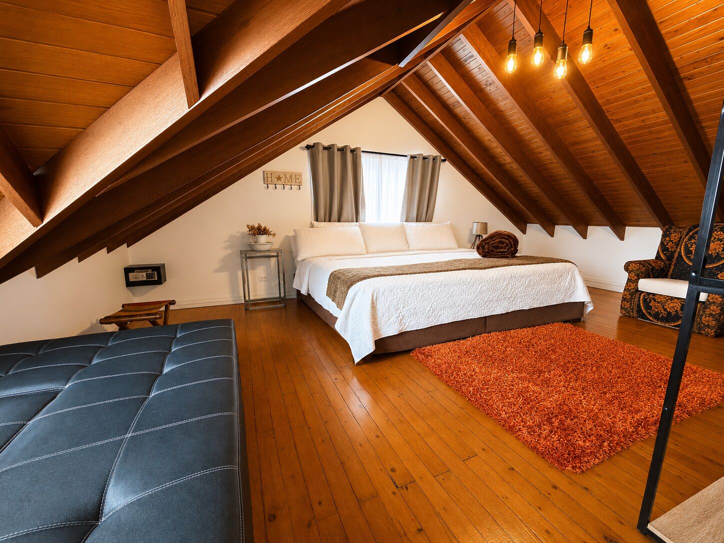 Un dormitorio con techo estilo loft, cama, sofá y sillón.