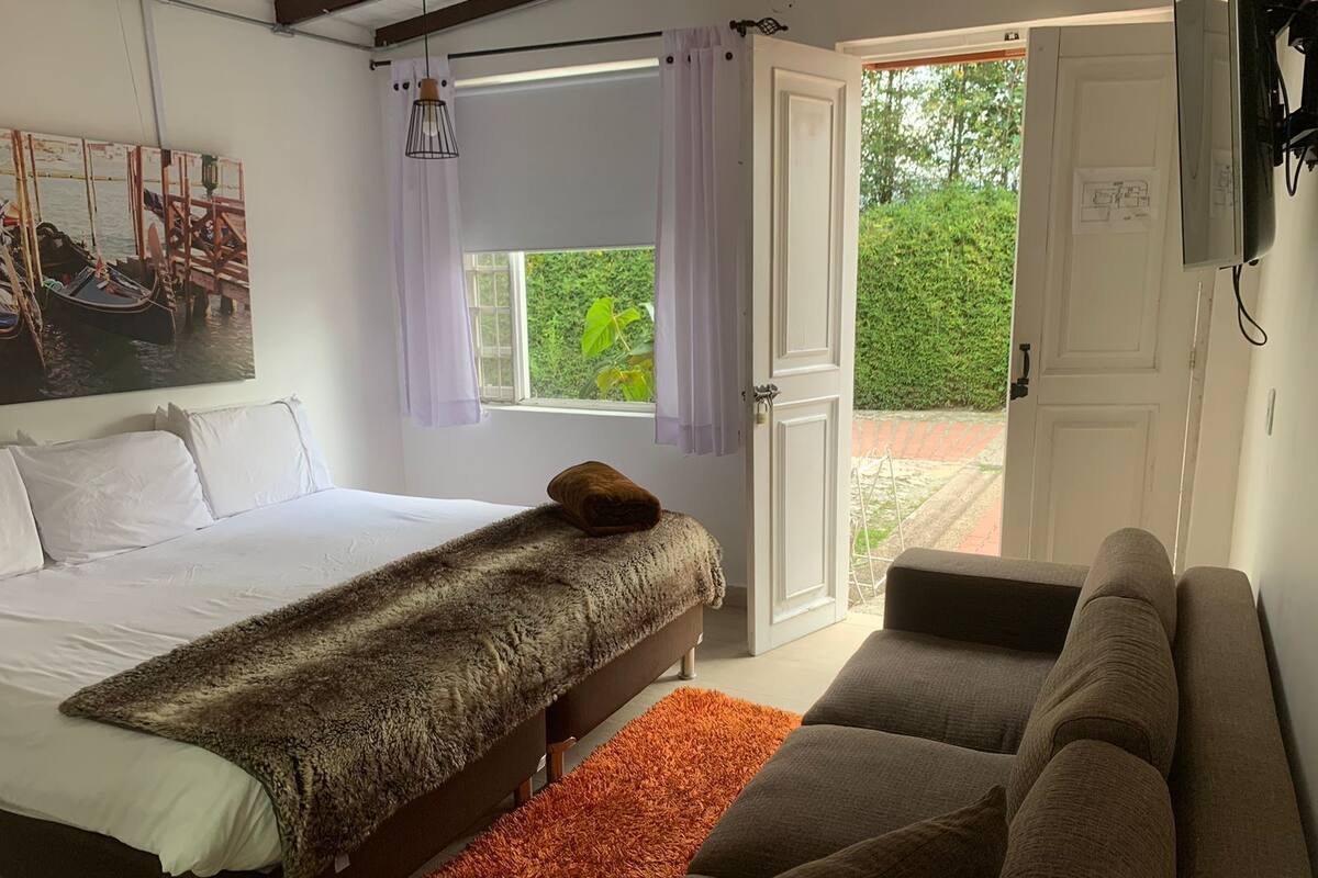 A bedroom with a bed, a sofa, a window with curtains, and a door leading outside.